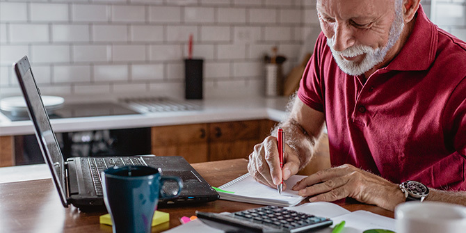 Man with open laptop, creating a budget on paper