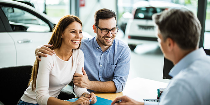 Man and woman talking with car salesman in a showroom