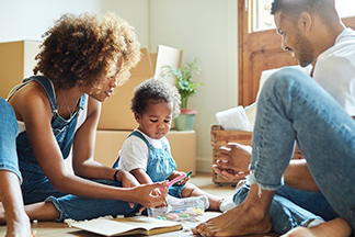 Parents and their toddler on the floor coloring together.