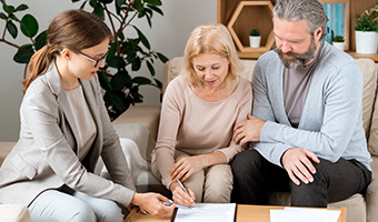 Young agent pointing at place for signature while mature client signs document.