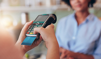 Young woman in a retail location paying by credit card. Focus on woman hands entering security pin in credit card reader.