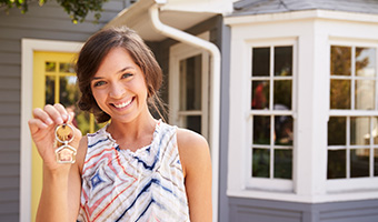 Smiling woman holding housekeys standing outside new home.