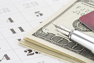 Ink pin laid over stack of $100 bills resting on a paper calendar