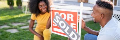 Couple kneeling next to a home sold sign.