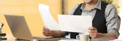 Man sitting a desk comparing two pieces of papers.