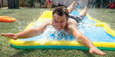 dad in back yard sliding on his stomach down a slip and slide