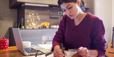woman looking at credit card making notes on paper with laptop nearby