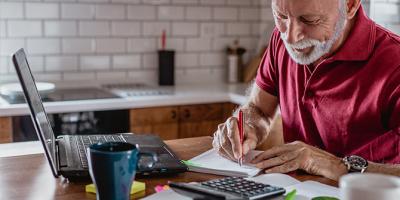 Man with open laptop, creating a budget on paper