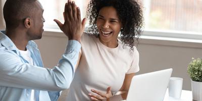 Couple sit near computer high-fiving