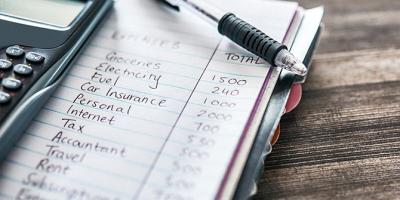 Handwritten budget in a notebook next to a calculator on a desk
