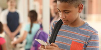 Young boy holding a smart phone and a backpack