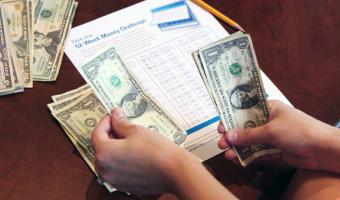 hands counting money on table in front of a 52-Week Money Challenge worksheet