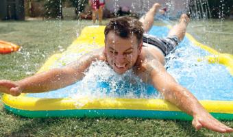 dad in back yard sliding on his stomach down a slip and slide