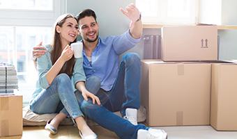 Couple sitting amid unpacked boxes in new home.