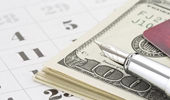 Ink pin laid over stack of $100 bills resting on a paper calendar