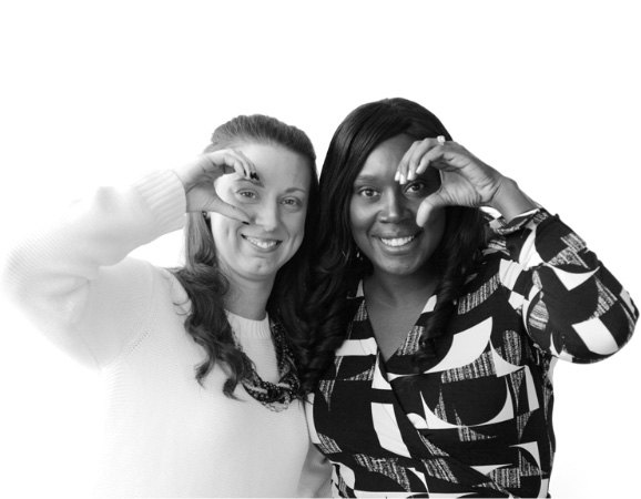 Two women smile and peek out through their hands, which form the letter “c”.