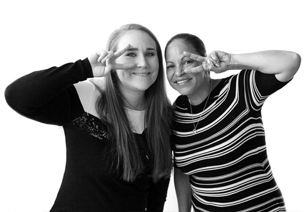 Women smiling while looking through their fingers which form vee-shapes.