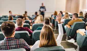 Back view of female student raising her hand to answer a question in a class lecture hall.