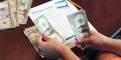 hands counting money on table in front of a 52-Week Money Challenge worksheet