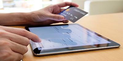 Hand holding credit card and typing payment information on tablet
